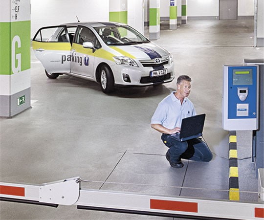 Ein Mitarbeiter der Vollmergruppe Parking bei der Problemlösung am Einlassautomaten eines Parkhauses mit dem Laptop.